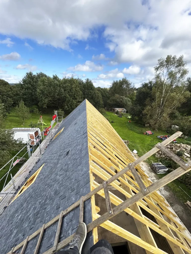 Faîtage d'une toiture en cours de pose à Quistinic, avec une partie en ardoise et une partie montrant la charpente en bois.