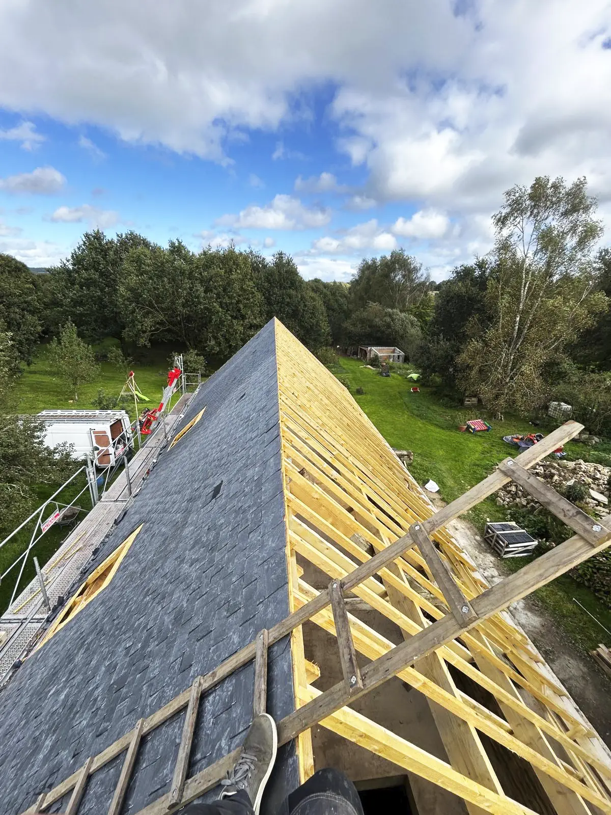 Faîtage d'une toiture en cours de pose à Quistinic, avec une partie en ardoise et une partie montrant la charpente en bois.