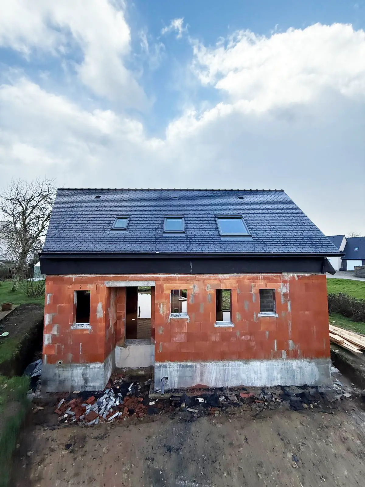 Maison neuve en briques à Camors avec sa toiture complète en ardoise et ses fenêtres de toit fraîchement posées.