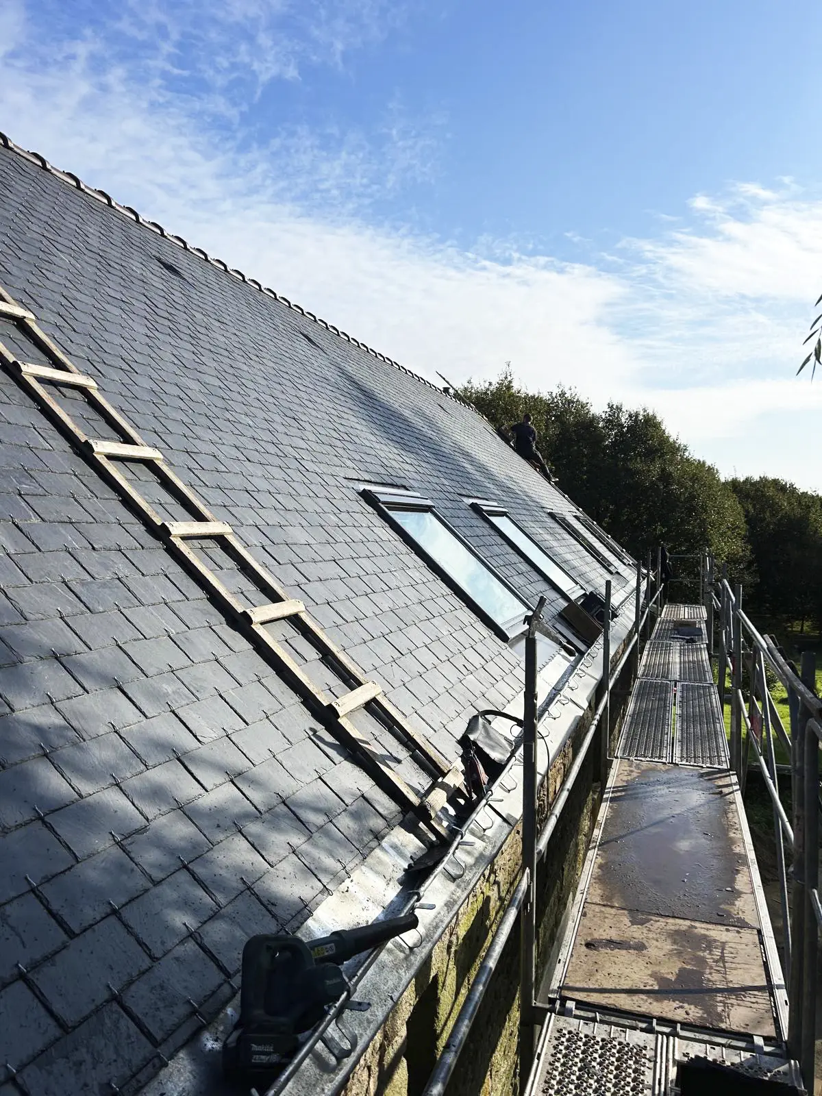 Couvreur réalisant les finitions sur une toiture en ardoise avec des fenêtres de toit, utilisant une échelle de couvreur.
