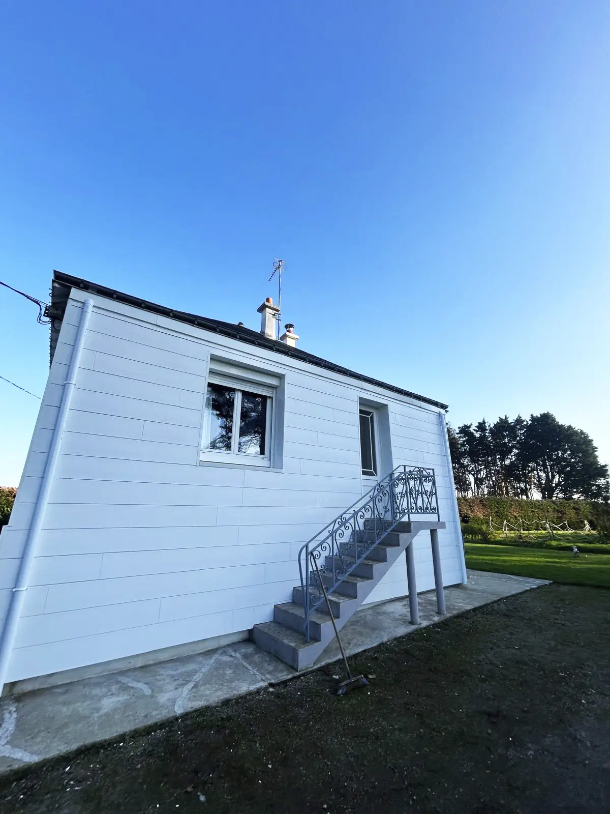 Façade d'une maison rénovée avec un bardage à claire-voie en PVC blanc et un escalier extérieur.