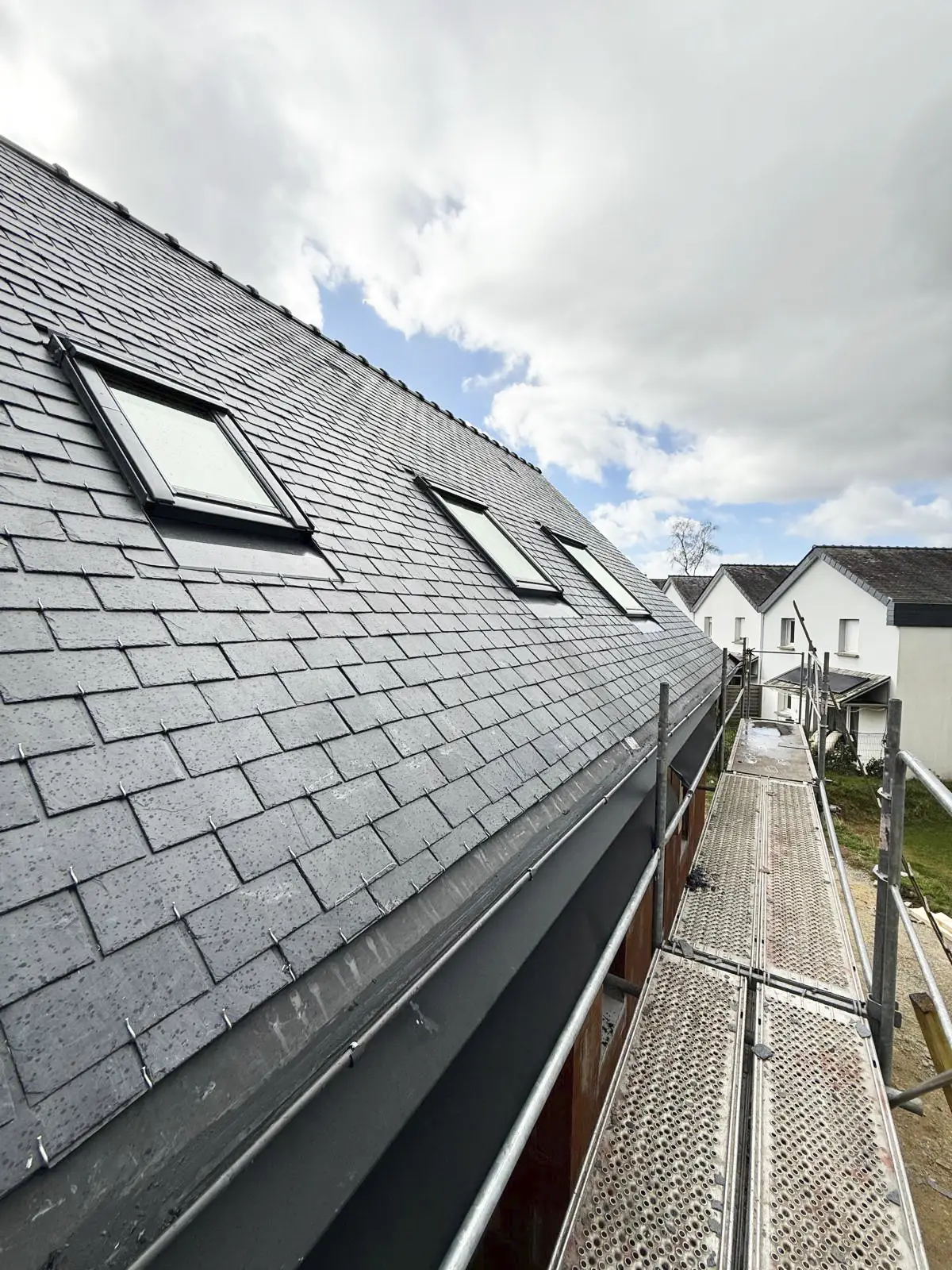 Gros plan sur trois fenêtres de toit installées sur une toiture en ardoise, vue depuis l'échafaudage.
