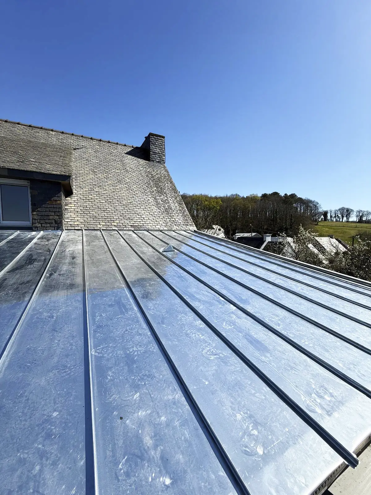 Toiture neuve en zinc à joint debout, raccordée à une toiture existante en ardoise.