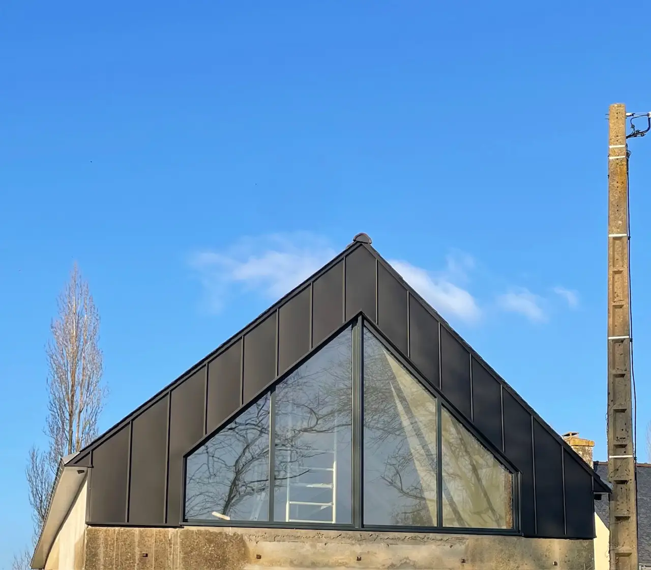 Pignon de maison moderne avec bardage en zinc noir à joint debout et grande verrière triangulaire réalisé par Rolland Toitures.